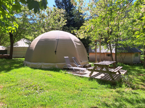 Wigwam dome tent with deck chairs and picnic table at Campsite Ushuaïa Villages Le Viaduc, France, in greenery.