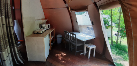 Interior de la cúpula Wigwam en Campsite Ushuaïa Villages Le Viaduc, Francia, con mesa, sillas y cocina.