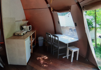 Interior de la cúpula Wigwam en Campsite Ushuaïa Villages Le Viaduc, Francia, con mesa, sillas y cocina.
