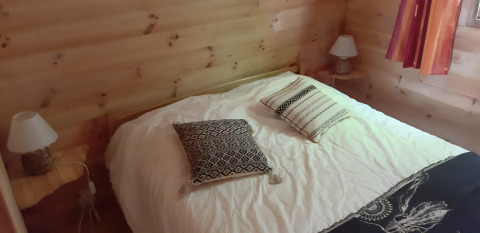 Schlafzimmer mit Holzwänden, Doppelbett, zwei Kissen, Nachttischen und Lampen im Ranch Chalet auf dem Campingplatz Ushuaïa Villages Le Viaduc.