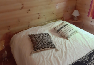 Schlafzimmer mit Holzwänden, Doppelbett, zwei Kissen, Nachttischen und Lampen im Ranch Chalet auf dem Campingplatz Ushuaïa Villages Le Viaduc.