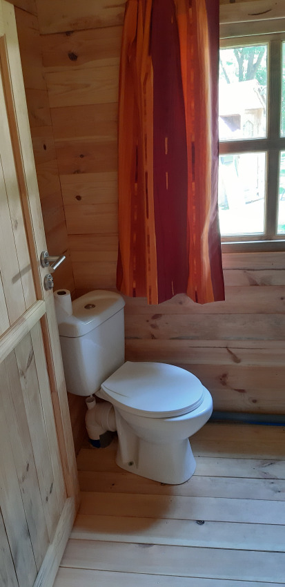 Toilette in einem holzvertäfelten Badezimmer mit Fenster und Vorhang im Ranch Chalet, Ushuaïa Villages Le Viaduc.
