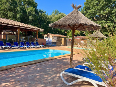 Swimming pool with blue loungers and thatched umbrellas at Campsite Le Luberon, Provence-Alpes-Côte d’Azur, France.