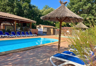Swimming pool with blue loungers and thatched umbrellas at Campsite Le Luberon, Provence-Alpes-Côte d’Azur, France.