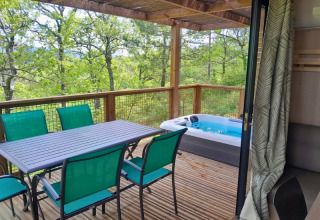 Wooden terrace at Campsite Le Luberon with green chairs, dining table, and hot tub facing the forest.