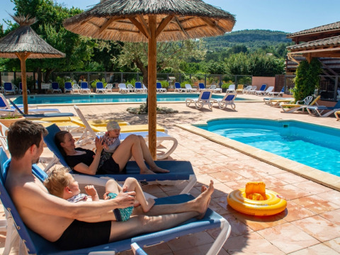 Family relaxing on poolside loungers at Campsite Le Luberon holiday park in Provence-Alpes-Côte d’Azur, France.