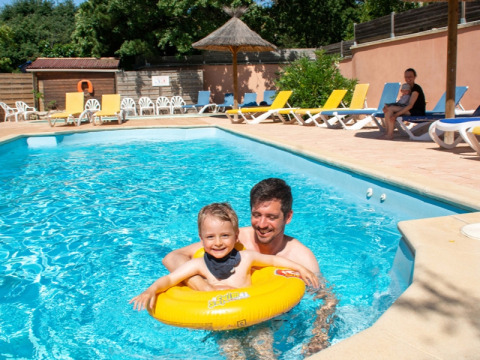 Papà e bambino si divertono in piscina al campeggio Le Luberon, Provenza, con sdraio al sole sullo sfondo.