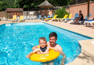 Papà e bambino si divertono in piscina al campeggio Le Luberon, Provenza, con sdraio al sole sullo sfondo.