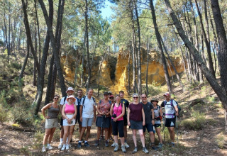 Un groupe de randonneurs pose devant des falaises ocres et des pins au camping Le Luberon en Provence.