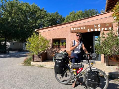 Un cycliste avec son vélo chargé devant le Camping Le Luberon en Provence, France, par une journée ensoleillée.