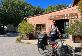 Un cycliste avec son vélo chargé devant le Camping Le Luberon en Provence, France, par une journée ensoleillée.