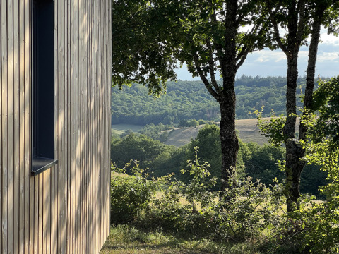 View from the Lodge at Campsite La Nouvelle Croze in France, showing trees and rolling green hills nearby.