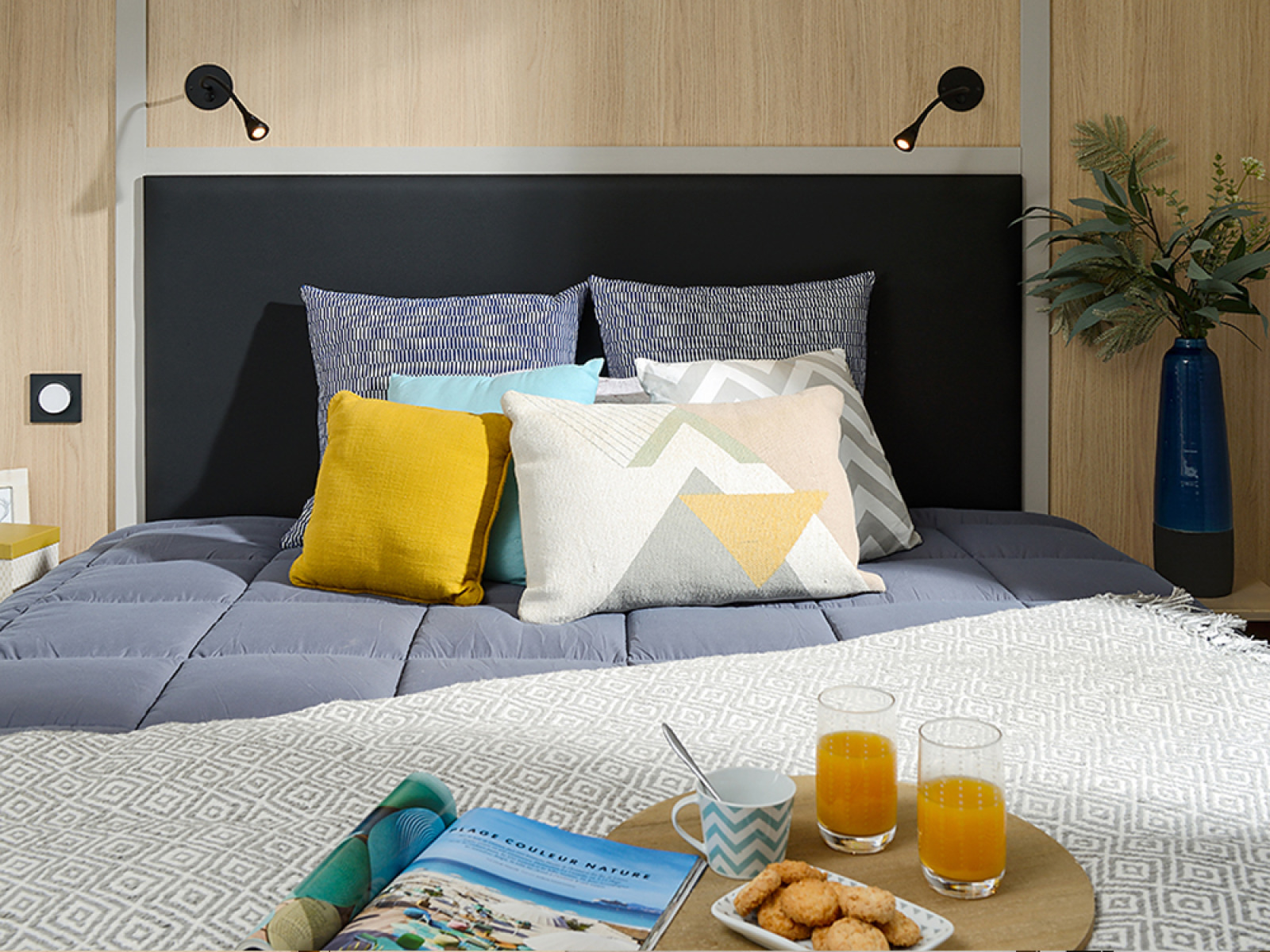 Moderne lodge-slaapkamer op Camping La Nouvelle Croze in Frankrijk met kussens en ontbijt op bed.