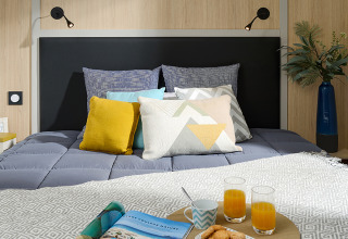Modern lodge bedroom at Campsite La Nouvelle Croze in France with stylish pillows, juice, and breakfast cookies.