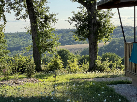Vista dalla lodge al Campeggio La Nouvelle Croze in Francia con alberi, prato e colline illuminate dal sole.