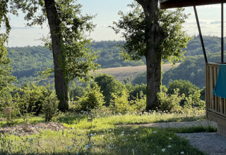 Vista dalla lodge al Campeggio La Nouvelle Croze in Francia con alberi, prato e colline illuminate dal sole.