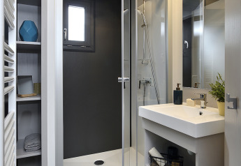 Modern lodge bathroom with glass shower, white sink, shelving, small window, and contemporary decor.