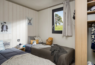 Cozy lodge bedroom with two single beds, window with outdoor view, and modern decor accents.