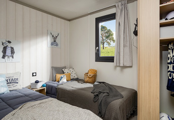 Cozy lodge bedroom with two single beds, window with outdoor view, and modern decor accents.