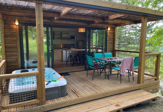 Cottage ‘Pantaïa’ al campeggio Le Luberon in Francia, con veranda coperta, vasca idromassaggio e tavolo da pranzo.