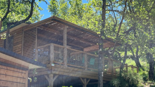 Treehouse Cottage «Séouvo» at Campsite Le Luberon in France, nestled among trees on a bright sunny day.