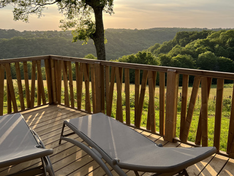 Wooden terrace with loungers overlooking green hills at Lodge on stilts, Campsite La Nouvelle Croze, France.