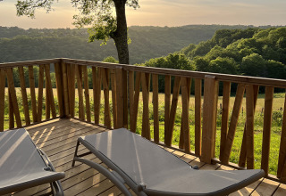Wooden terrace with loungers overlooking green hills at Lodge on stilts, Campsite La Nouvelle Croze, France.