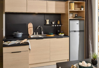 Kitchenette moderne dans une Lodge sur pilotis au Camping La Nouvelle Croze en France, bois clair et noir élégant.