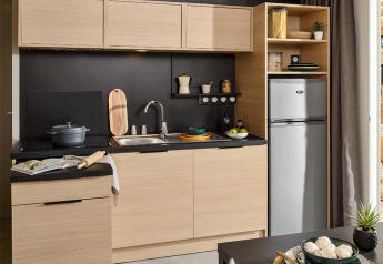 Modern kitchenette at Lodge on stilts at Campsite La Nouvelle Croze in France with wood cabinets and black accents.