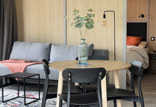 Gemütliche Lodge mit Essecke, Sofa und Schlafzimmer im Hintergrund, auf dem Campingplatz La Nouvelle Croze, Frankreich.