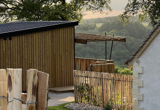 View of the Lodge on stilts at Campsite La Nouvelle Croze, France, surrounded by lush green hills.