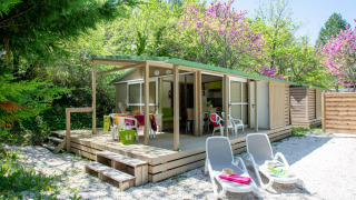 Veduta esterna del Cottage Lavande al campeggio Le Luberon in Francia con veranda, sedie e lettini.