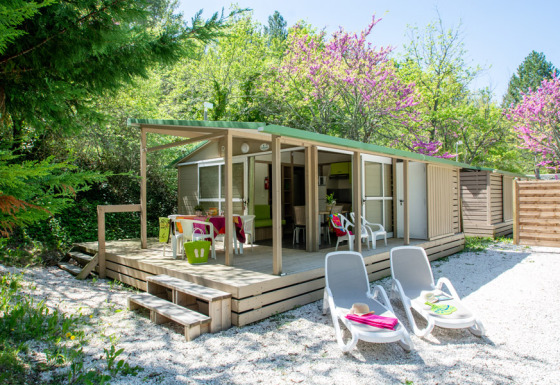 Veduta esterna del Cottage Lavande al campeggio Le Luberon in Francia con veranda, sedie e lettini.