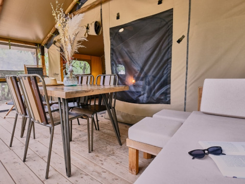 Zona pranzo interna con tavolo in legno, sedie e divano in una tenda glamping al Domaine des Chênes Blancs.