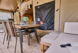 Indendørs spiseområde med træbord, stole og dekorationer i et glampingtelt i Domaine des Chênes Blancs.