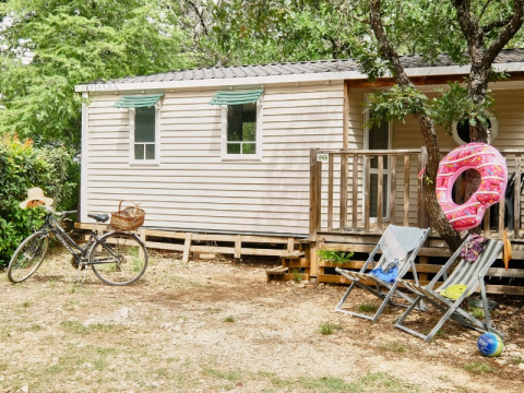 Casa mobile al Domaine des Chênes Blancs con bicicletta, sdraio e salvagente, immersa nel verde.