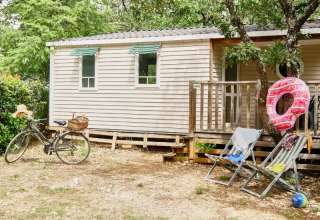 Casa móvil en Domaine des Chênes Blancs con bicicleta, tumbonas y flotador, rodeada de árboles verdes.