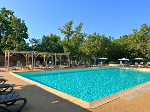 Piscina all'aperto con lettini e ombrelloni presso Domaine des Chênes Blancs in Provenza, Francia, tra alberi.