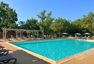 Piscina all'aperto con lettini e ombrelloni presso Domaine des Chênes Blancs in Provenza, Francia, tra alberi.