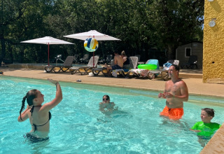 Familie spielt mit einem Wasserball im Pool am Domaine des Chênes Blancs, umgeben von Sonne und Liegen.
