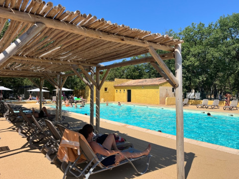 Piscine au Domaine des Chênes Blancs en Provence, France, avec des vacanciers sous les pergolas en bois.