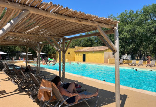 Piscina al Domaine des Chênes Blancs in Provenza, Francia, con ospiti rilassati sotto pergolati in legno.