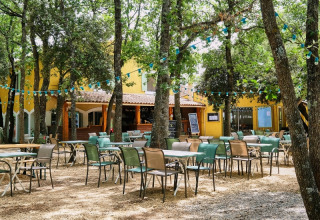 Spazio esterno del caffè al Domaine des Chênes Blancs in Provenza, con tavoli tra alberi e luci colorate.