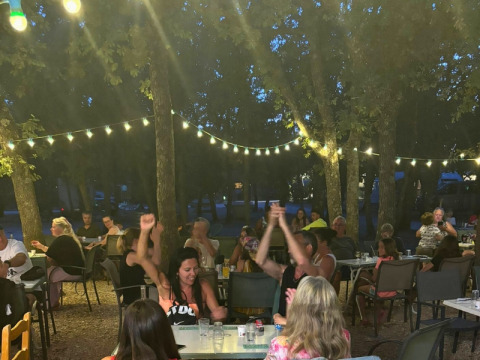 Avondsfeer in Domaine des Chênes Blancs met mensen die gezellig buiten eten onder lichtjes en bomen.