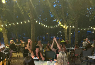 Noche en Domaine des Chênes Blancs: personas cenando y celebrando bajo luces y árboles al aire libre.
