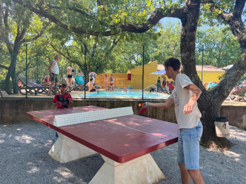 Dos personas juegan tenis de mesa al aire libre junto a una piscina en Domaine des Chênes Blancs, Provenza, Francia.
