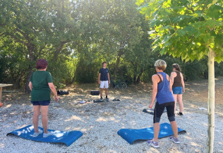 Buiten fitnessactiviteit in Domaine des Chênes Blancs, een vakantiepark met matten en instructeur onder bomen.