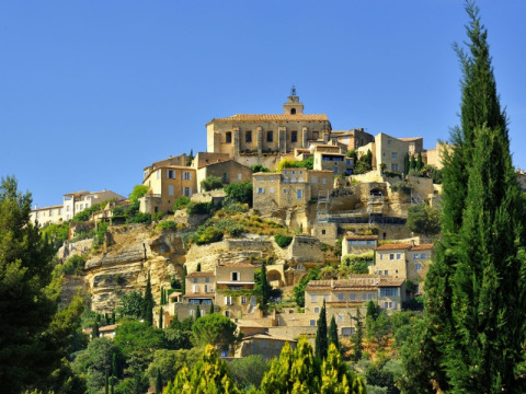 Case in pietra sulla collina di Saint-Saturnin-lès-Apt in Provenza, circondate da vegetazione sotto cielo limpido.