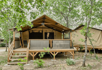 Safari-teltet Lodge COSY omgivet af træer, hævet på en platform med veranda og trapper, set udefra.