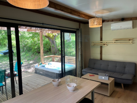 Vista interna di un cottage moderno con divano, tavolo da pranzo e vasca idromassaggio esterna a Camping Le Luberon, Francia.